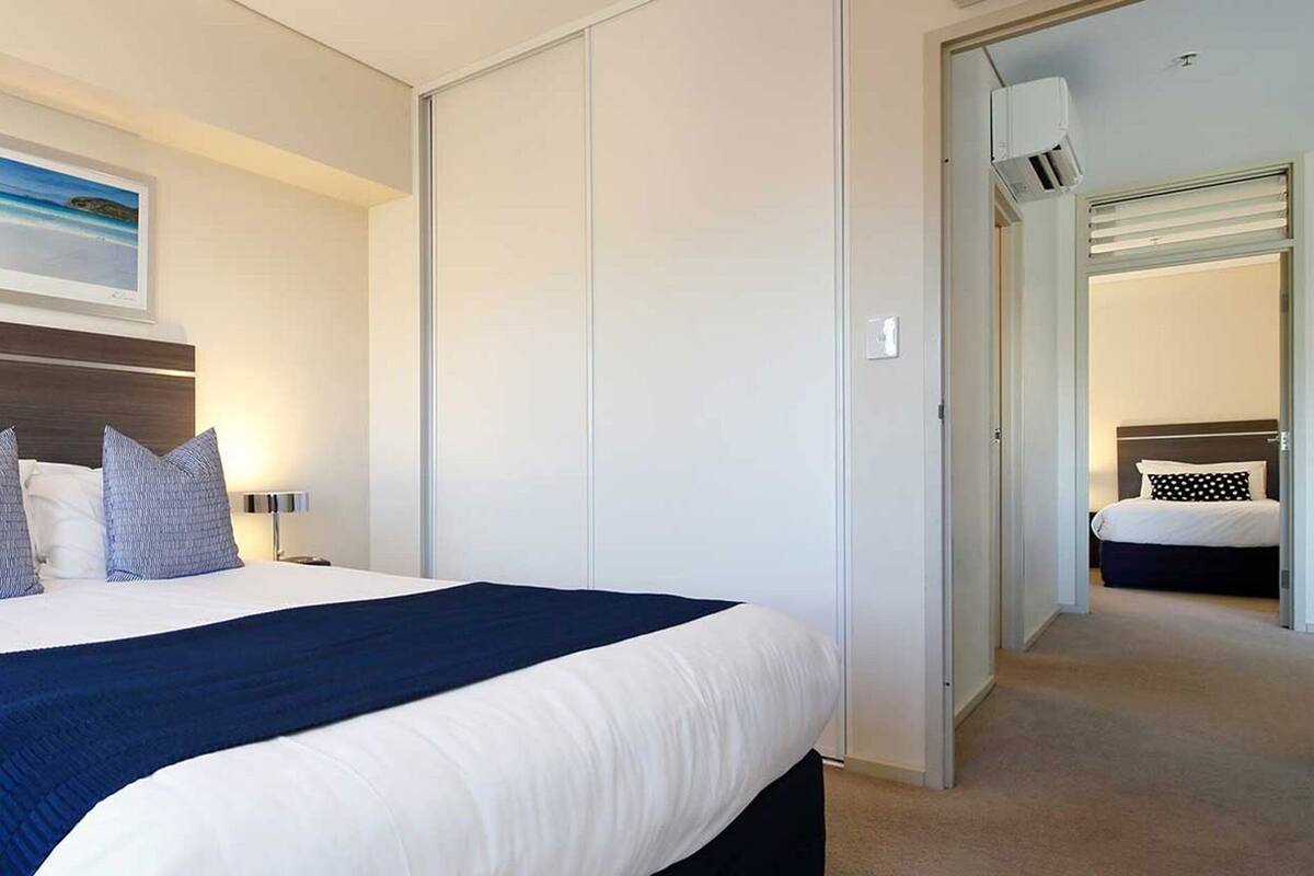 Una habitación de hotel moderna con una cama grande, una mesita de noche, un equipo de aire acondicionado instalado en la pared y un cuadro enmarcado sobre la cama.