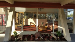 A modern interior with a wooden bench, a table, and a chair. There is a window with a view of the street outside. - Willow Tree Lodge (Fullerton)