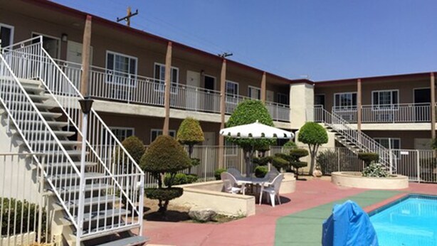 A multi-story motel with a swimming pool, outdoor seating, and a staircase leading to the upper floors. - Willow Tree Lodge (Fullerton)