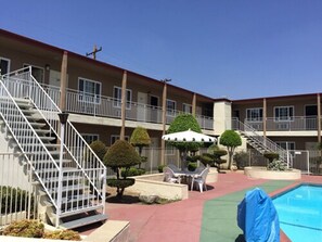 A multi-story motel with a swimming pool, outdoor seating, and a staircase leading to the upper floors. - Willow Tree Lodge (Fullerton)