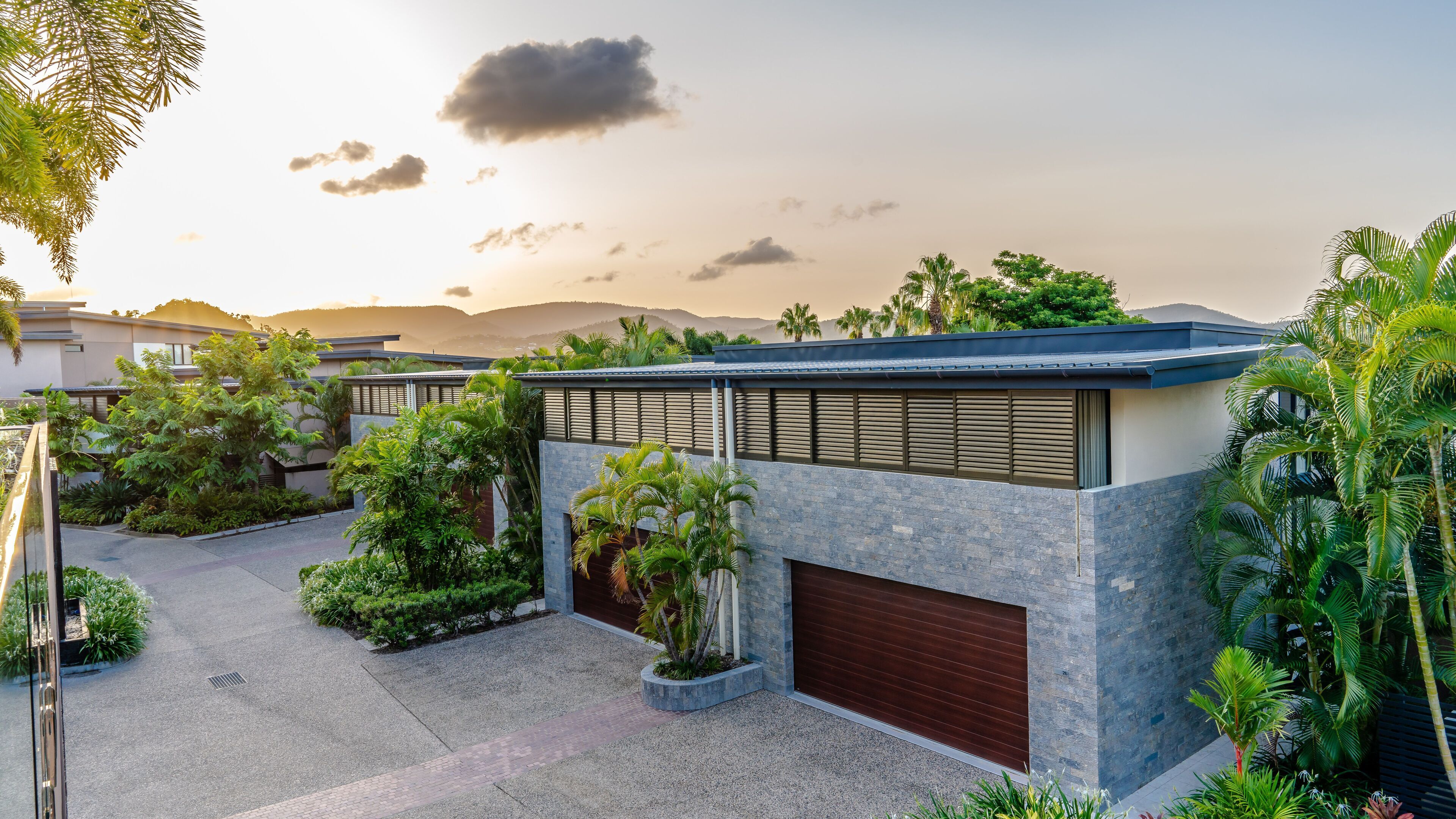 A modern building with a flat roof, surrounded by lush greenery and palm trees.