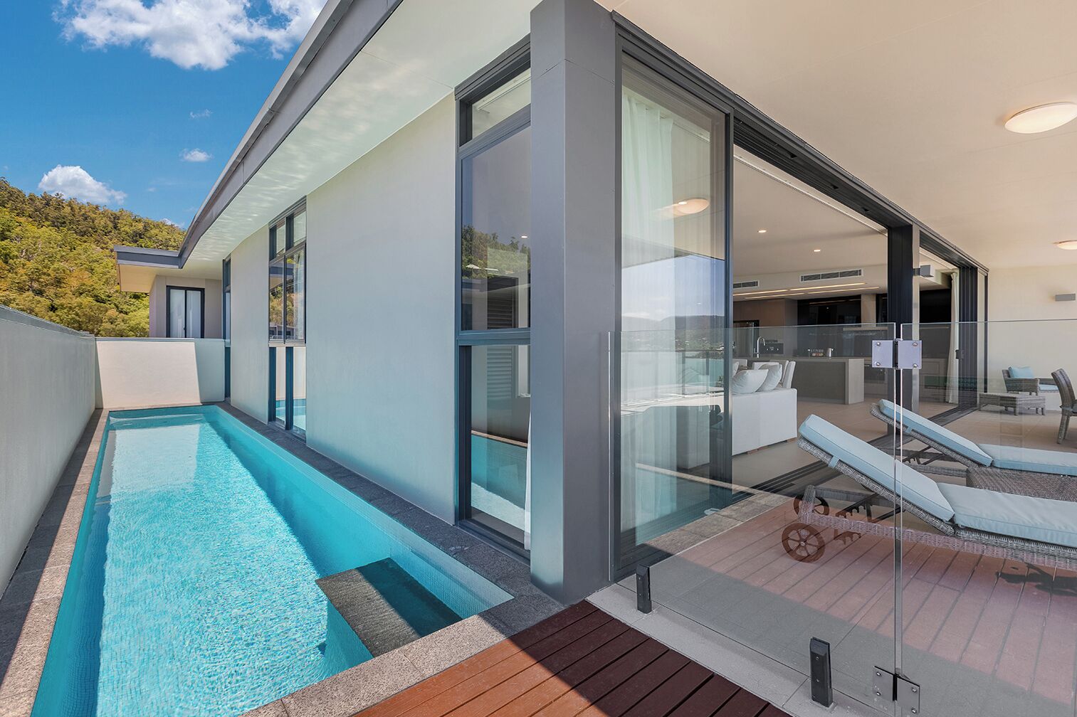 A modern house with a swimming pool, glass doors, and a patio with lounge chairs.
