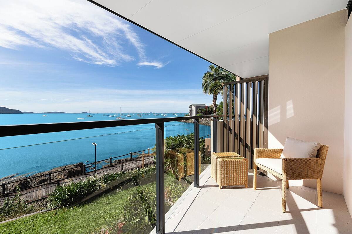Un balcon agrémenté de meubles en osier, une vue sur la mer et un ciel dégagé.