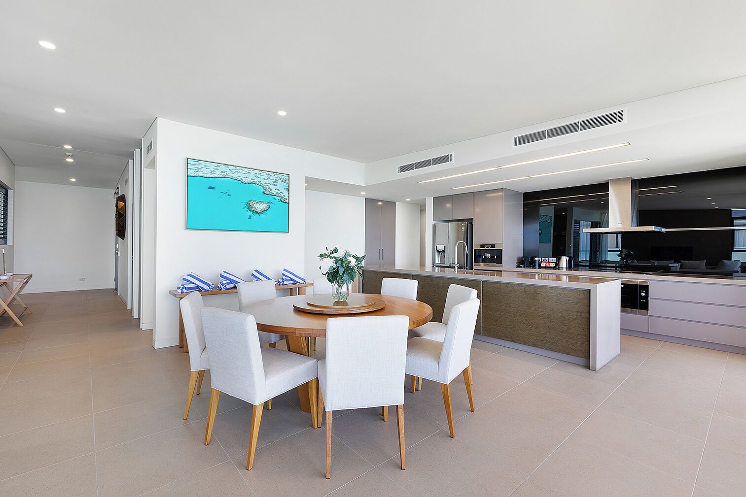 Una cocina moderna con una isla central, una zona de comedor con una mesa redonda y sillas, y un cuadro grande en la pared.
