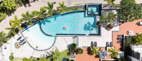 An aerial view of a resort with a large pool, sun loungers, and palm trees.