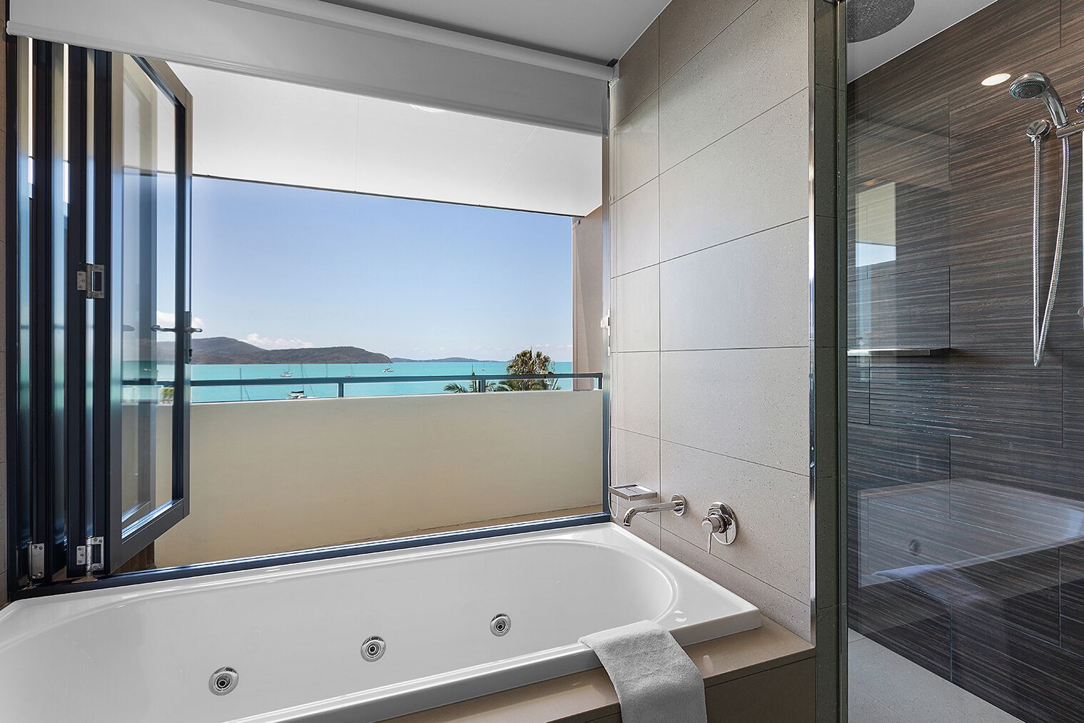 Un baño moderno con bañera, ducha y un balcón con vistas al mar.