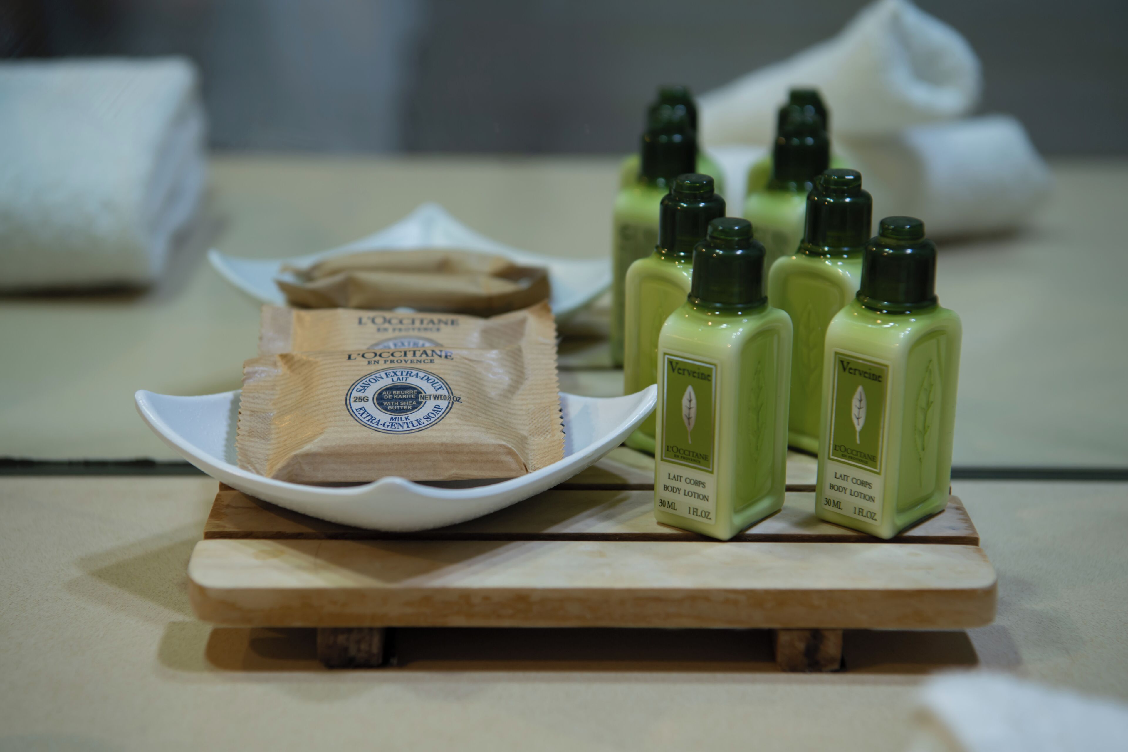 A tray with body lotion bottles and a bar of soap on a wooden surface.