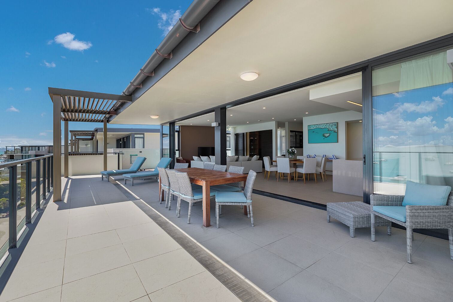 A balcony with a dining area, lounge chairs, and a pergola.