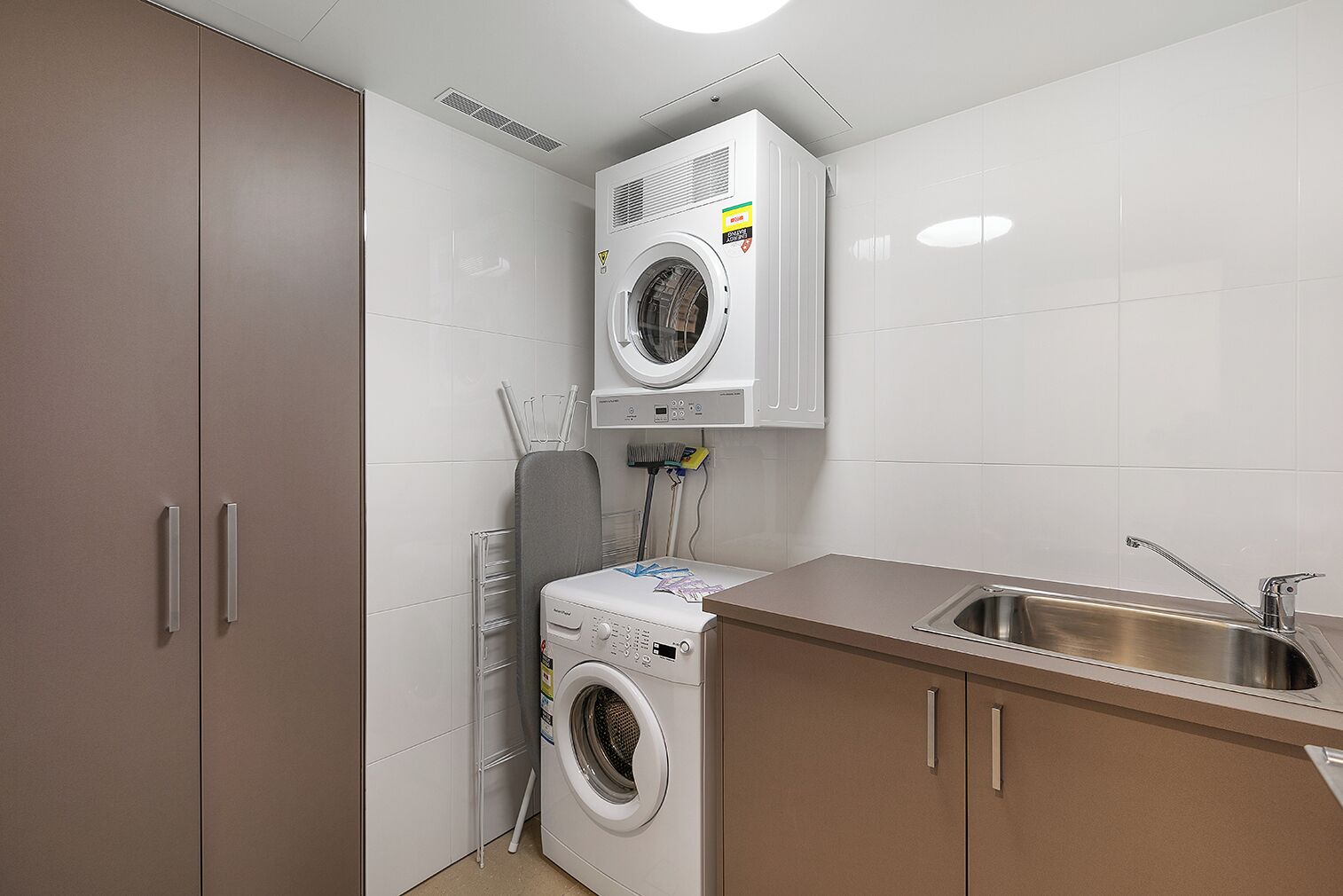 A compact laundry room with a washing machine, dryer, and a sink.