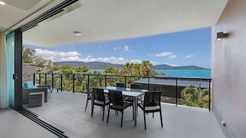 A balcony with a table and chairs, offering a view of the sea and mountains.