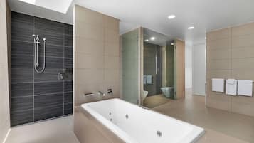 A modern bathroom with a large bathtub, a glass-enclosed shower, and a toilet visible through the glass.