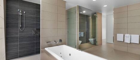 A modern bathroom with a large bathtub, a glass-enclosed shower, and a toilet visible through the glass.