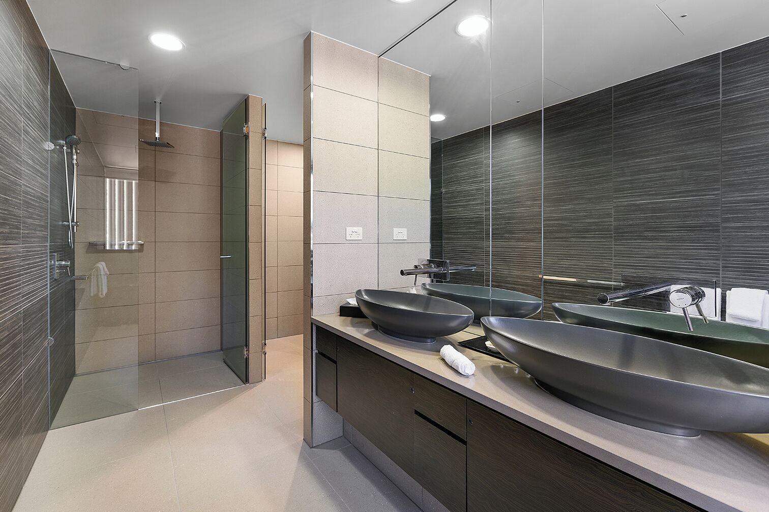 A modern bathroom with a walk-in shower, two large vessel sinks, and a large mirror.