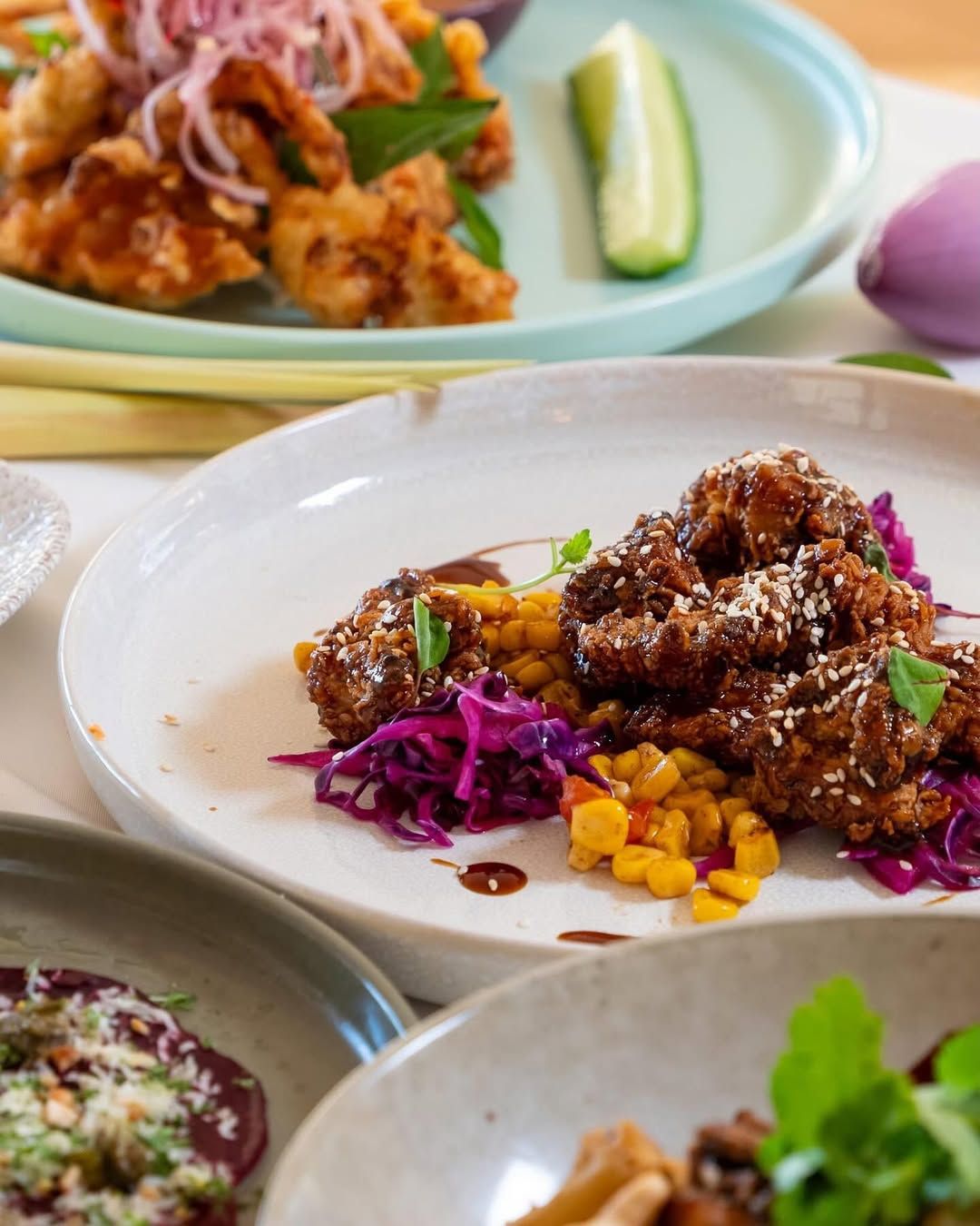A variety of dishes on a table, including meatballs with sesame seeds, corn, and purple cabbage.