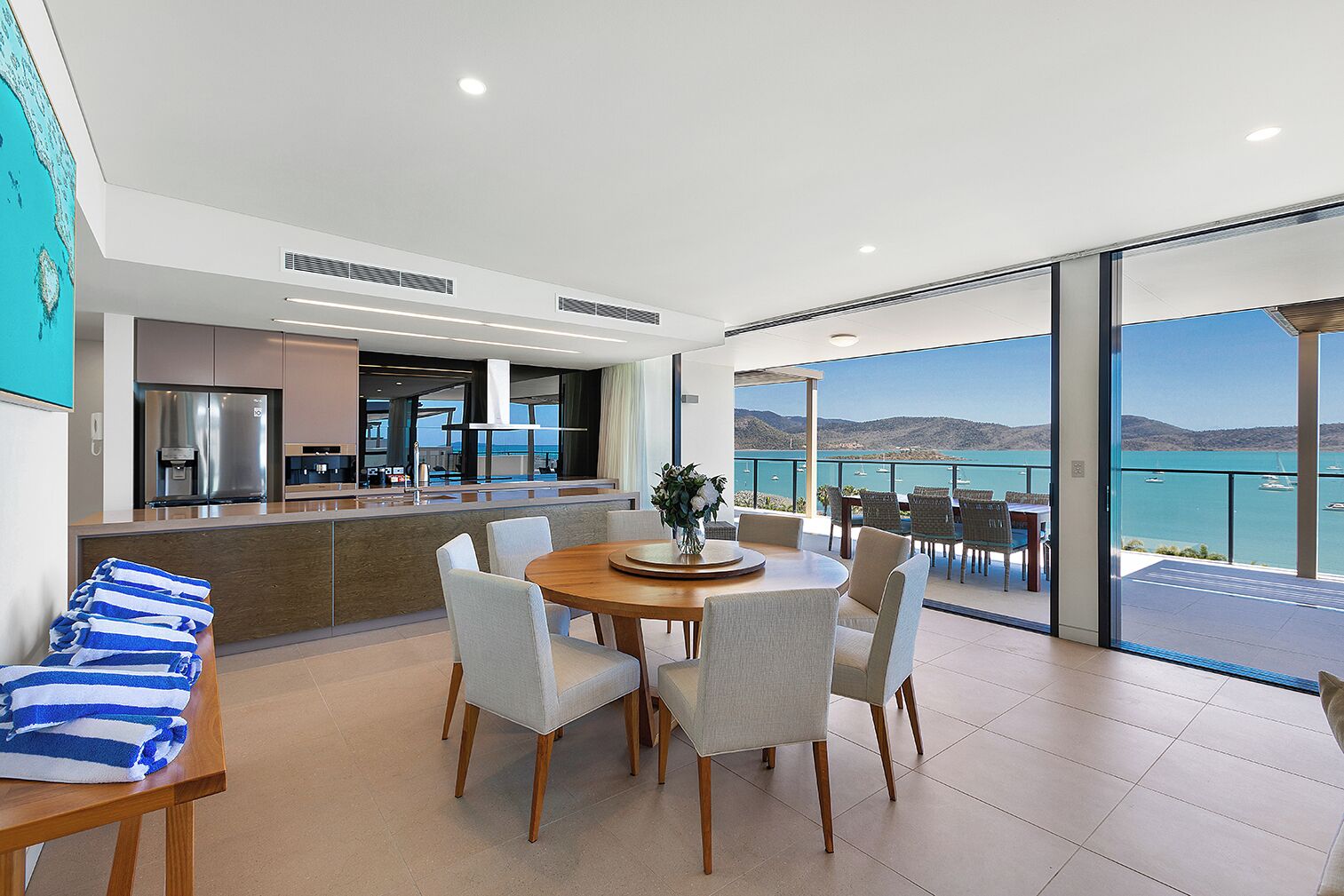 Una cocina moderna con una isla central, un área de comedor con una mesa redonda y sillas, y un balcón con vistas al mar.