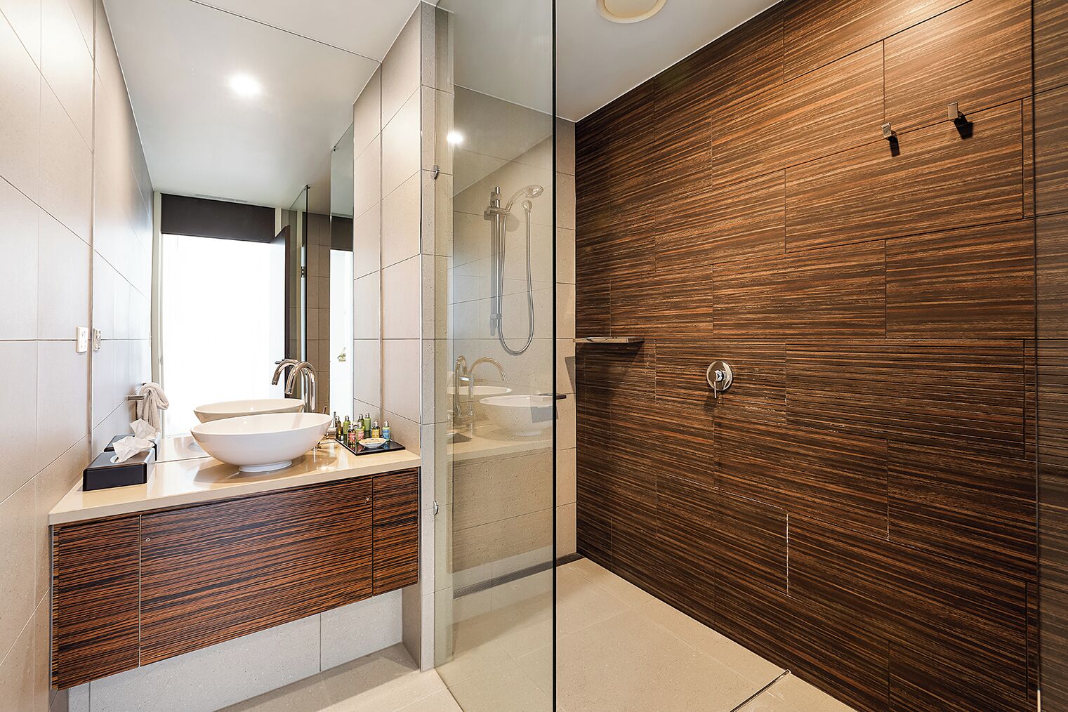 A modern bathroom with a large sink, a glass shower enclosure, and a wooden accent wall.