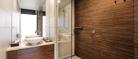 A modern bathroom with a large sink, a glass shower enclosure, and a wooden accent wall.