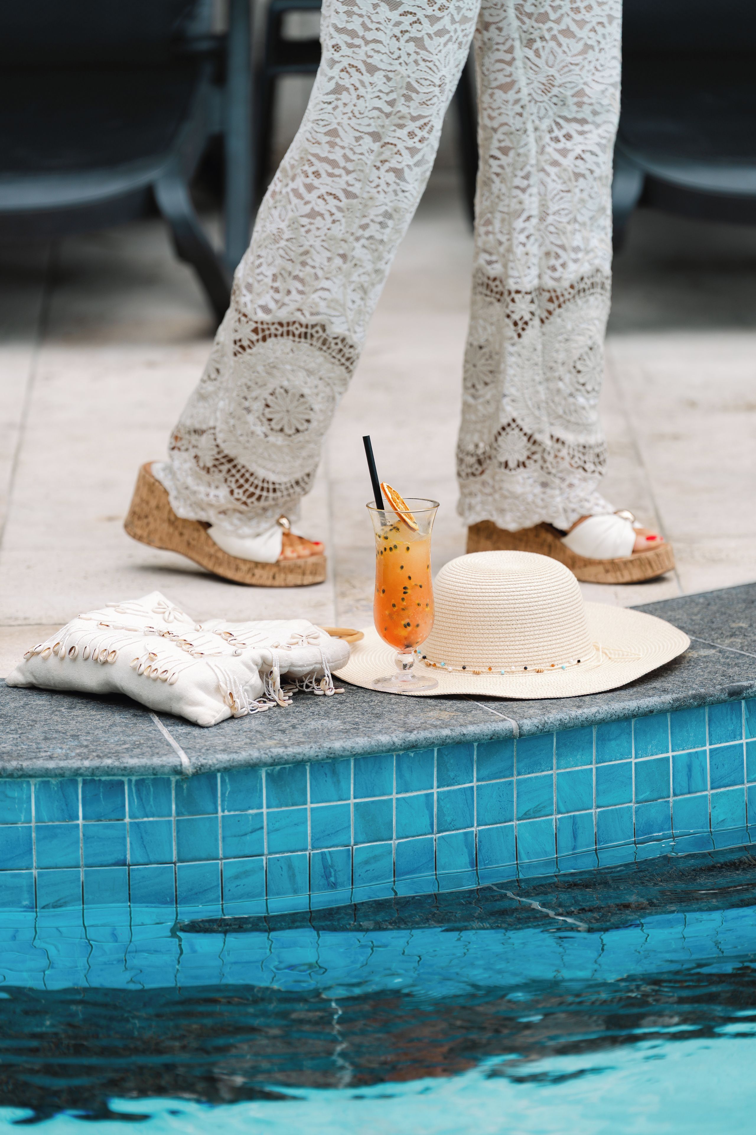 A poolside setting with a drink, a hat, and a cushion.