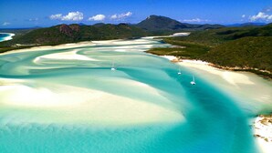 Un paysage côtier caractérisé par une eau turquoise cristalline, de plages de sable blanc et quelques voiliers.