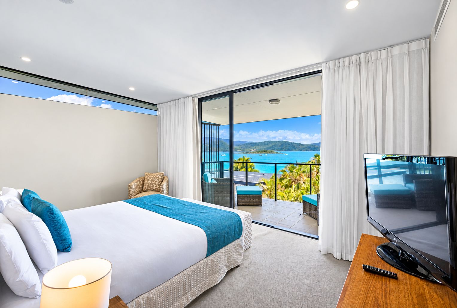Habitación de hotel con cama, televisión, balcón y vistas al mar, además de una silla.