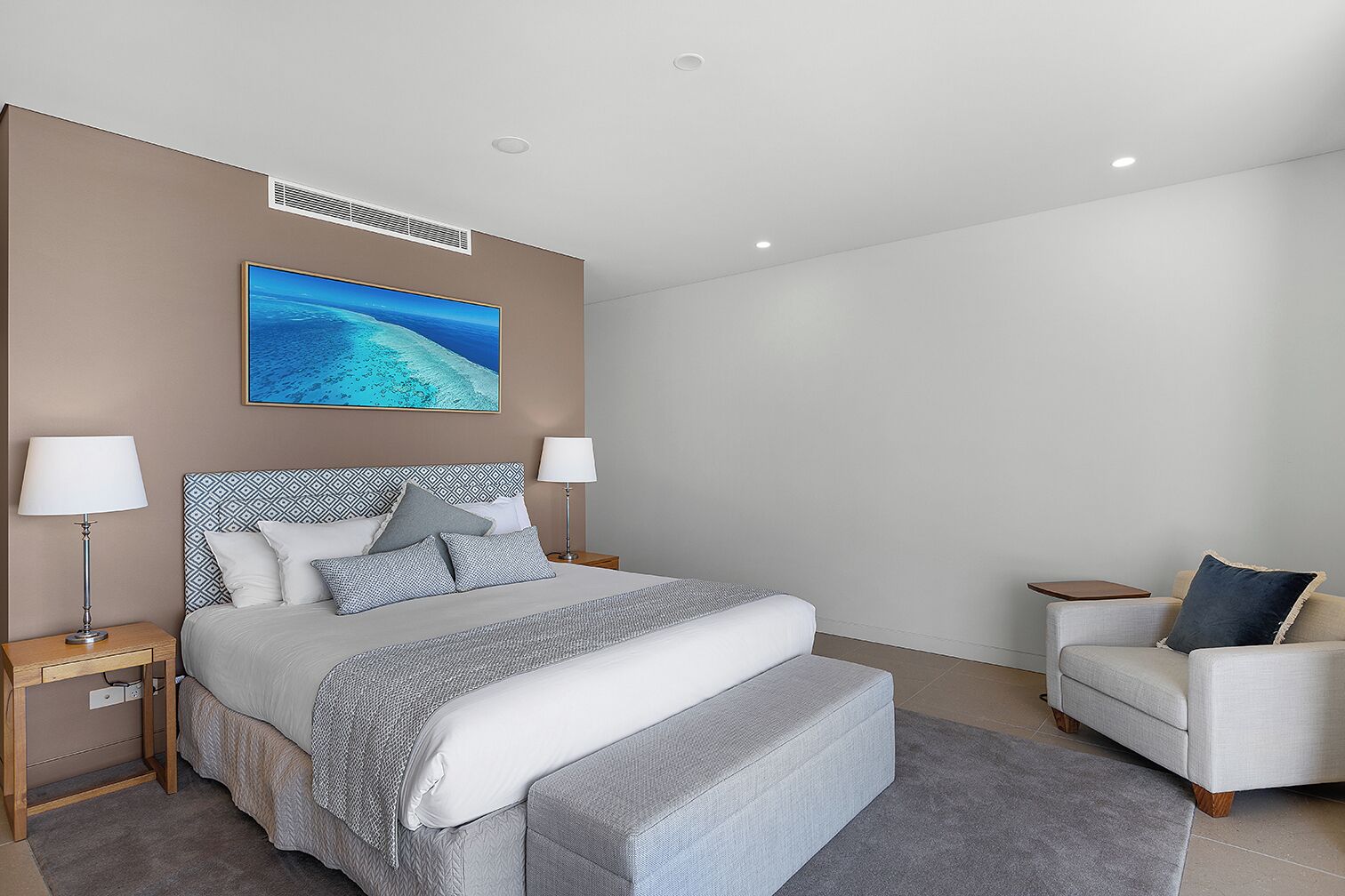 A modern bedroom with a large bed, two bedside tables, a nightstand, a sofa, and a wall-mounted air conditioning unit.