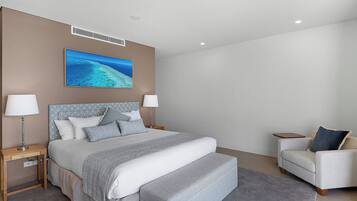 Un dormitorio moderno con una cama grande, dos mesitas de noche, un tocador, un sofá y un equipo de aire acondicionado instalado en la pared.