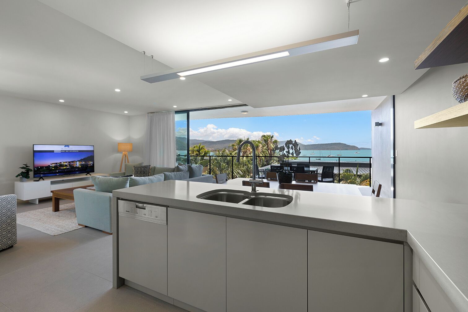 A modern kitchen with a large island, a dining area with a view, and a living room with a TV.