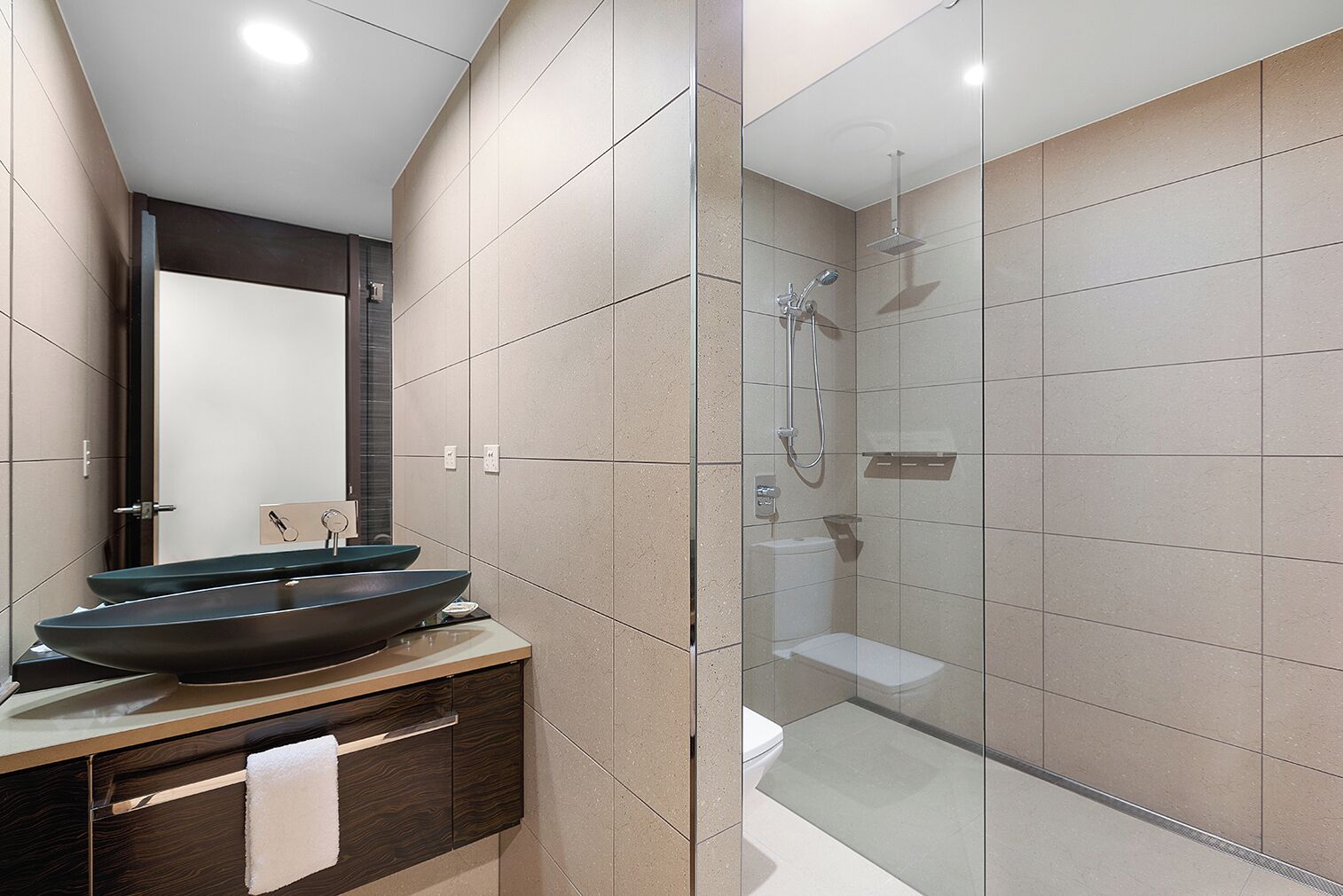 A modern bathroom with a large mirror, a vessel sink, a glass-enclosed shower, and a wooden vanity.