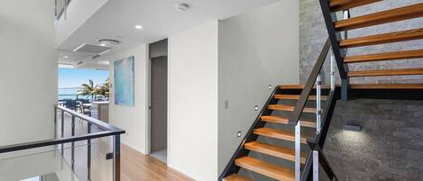 Un intérieur moderne avec un escalier en bois, des rampes en verre et une vue sur la mer.