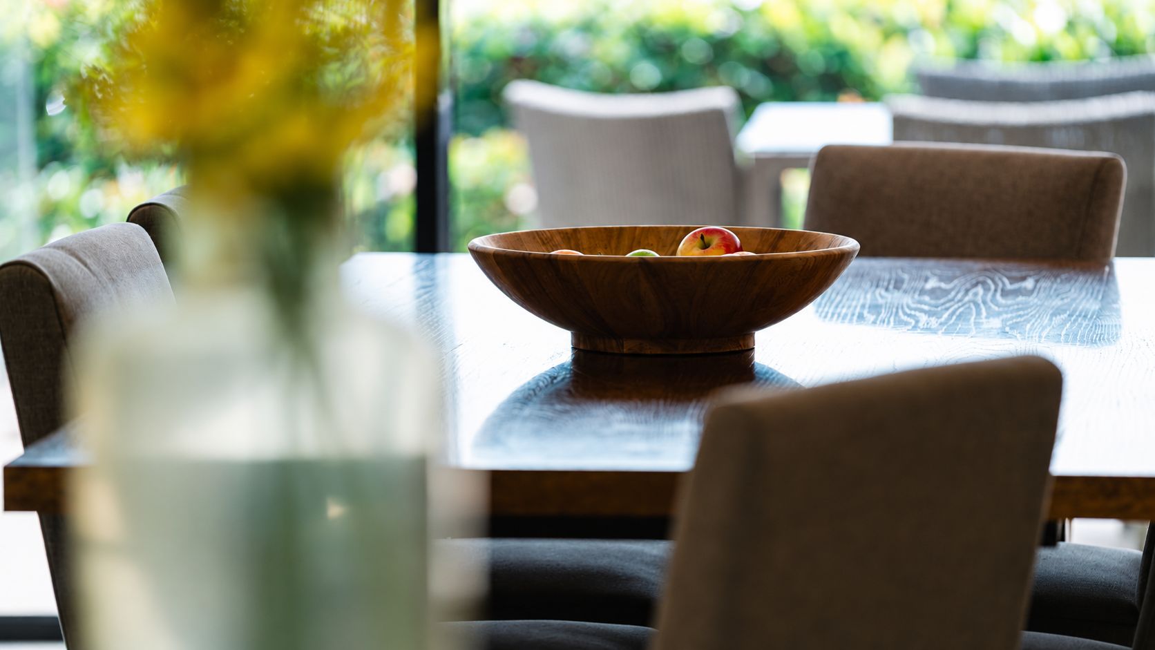 Uma mesa de jantar com uma tigela de madeira e um vaso com flores.