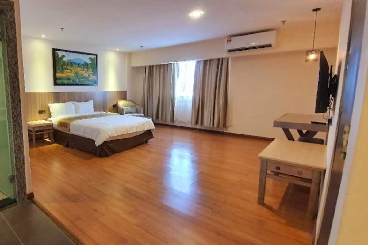 A hotel room with a bed, bedside table, and a small desk. There is a bathroom with a sink and mirror.