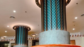 Um saguão com duas colunas cilíndricas grandes, cobertas com tecido estampado e base refletora.