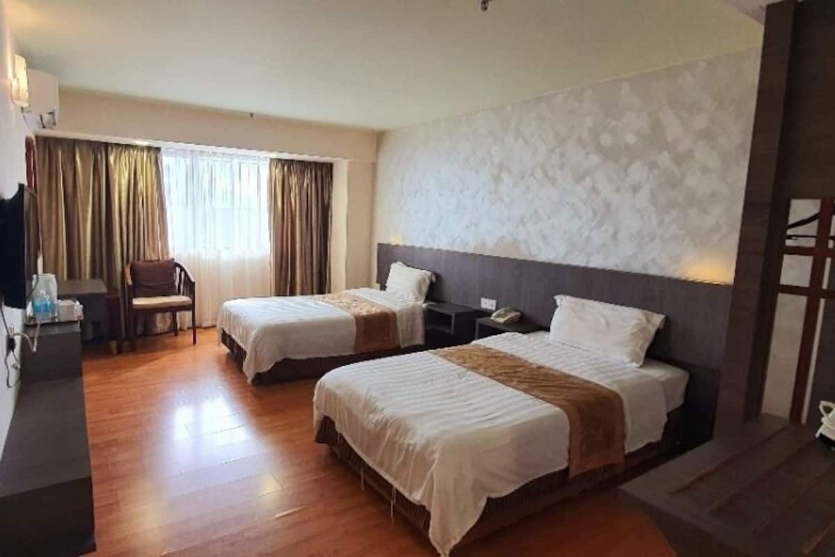 A hotel room with two beds, a desk, a chair, and a TV.