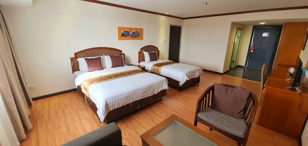 A hotel room with two beds, a small table, a chair, and a painting on the wall.