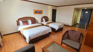 A hotel room with two beds, a small table, a chair, and a painting on the wall.
