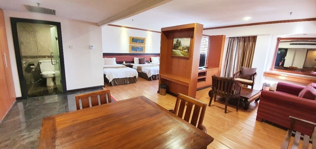 A hotel room with a wooden dining table, two single beds, a red sofa, and a TV.