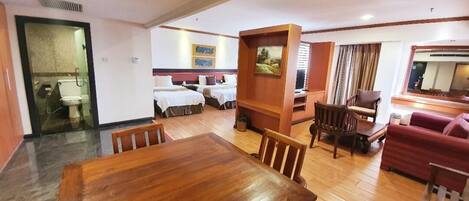 A hotel room with a wooden dining table, two single beds, a red sofa, and a TV.
