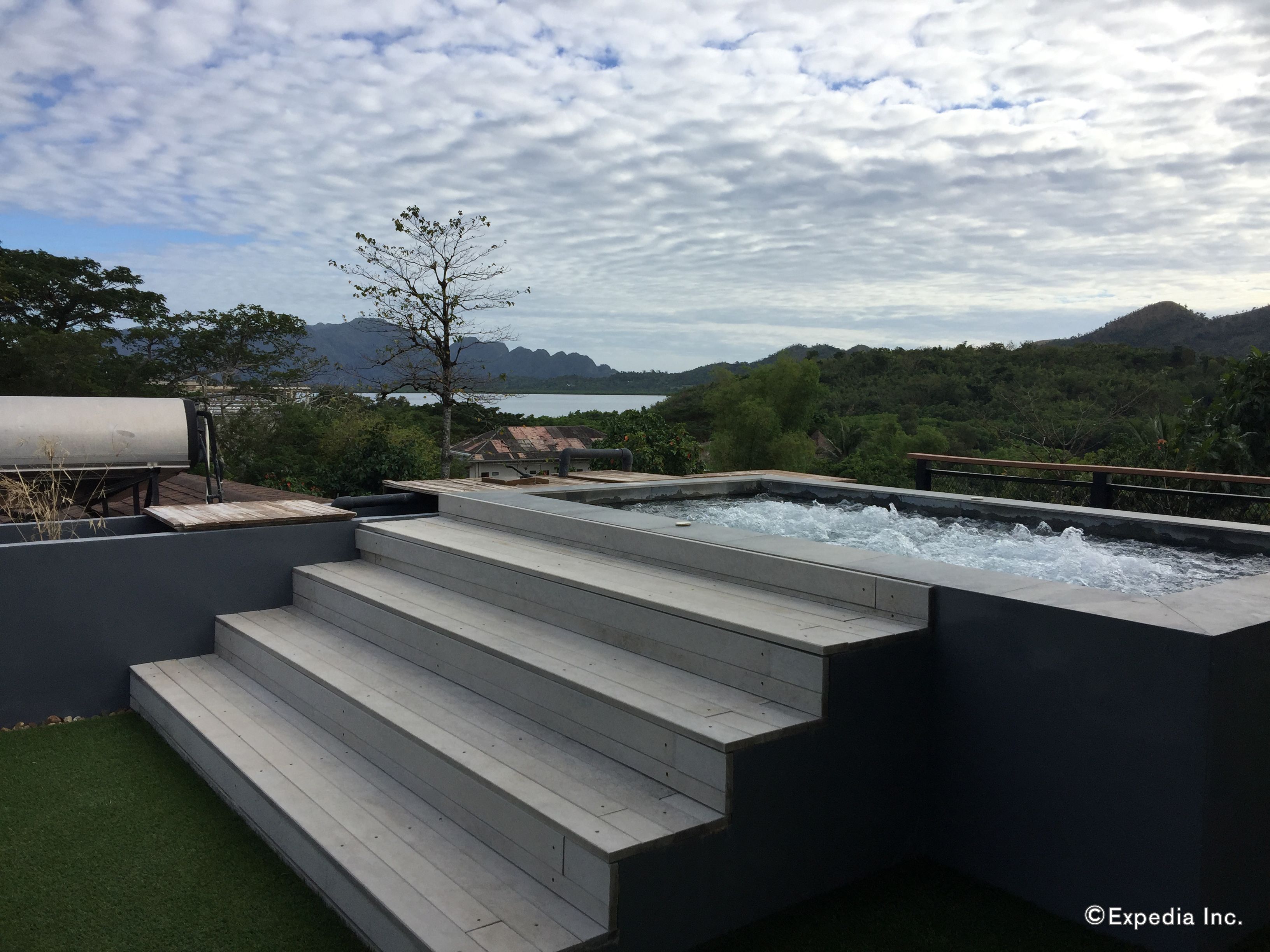 A hot tub with steps leading to it, surrounded by a pool and a view of mountains and a lake.