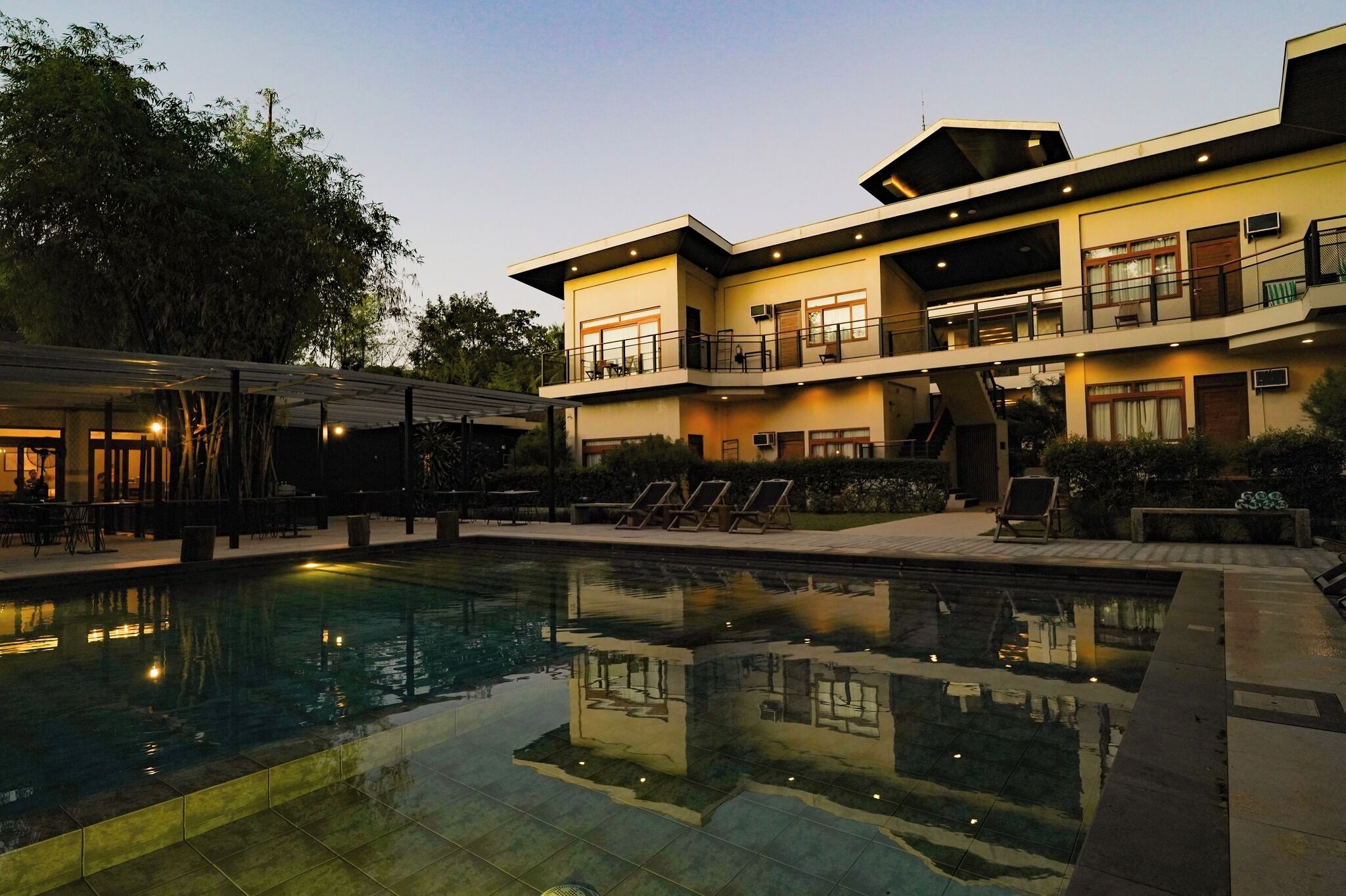 Un hotel moderno con piscina, mobiliario exterior y una zona de balcón bien iluminada.