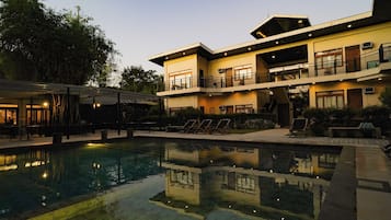 Un hotel moderno con piscina, mobiliario exterior y una zona de balcón bien iluminada.