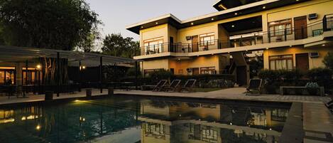 Un hotel moderno con piscina, mobiliario exterior y una zona de balcón bien iluminada.