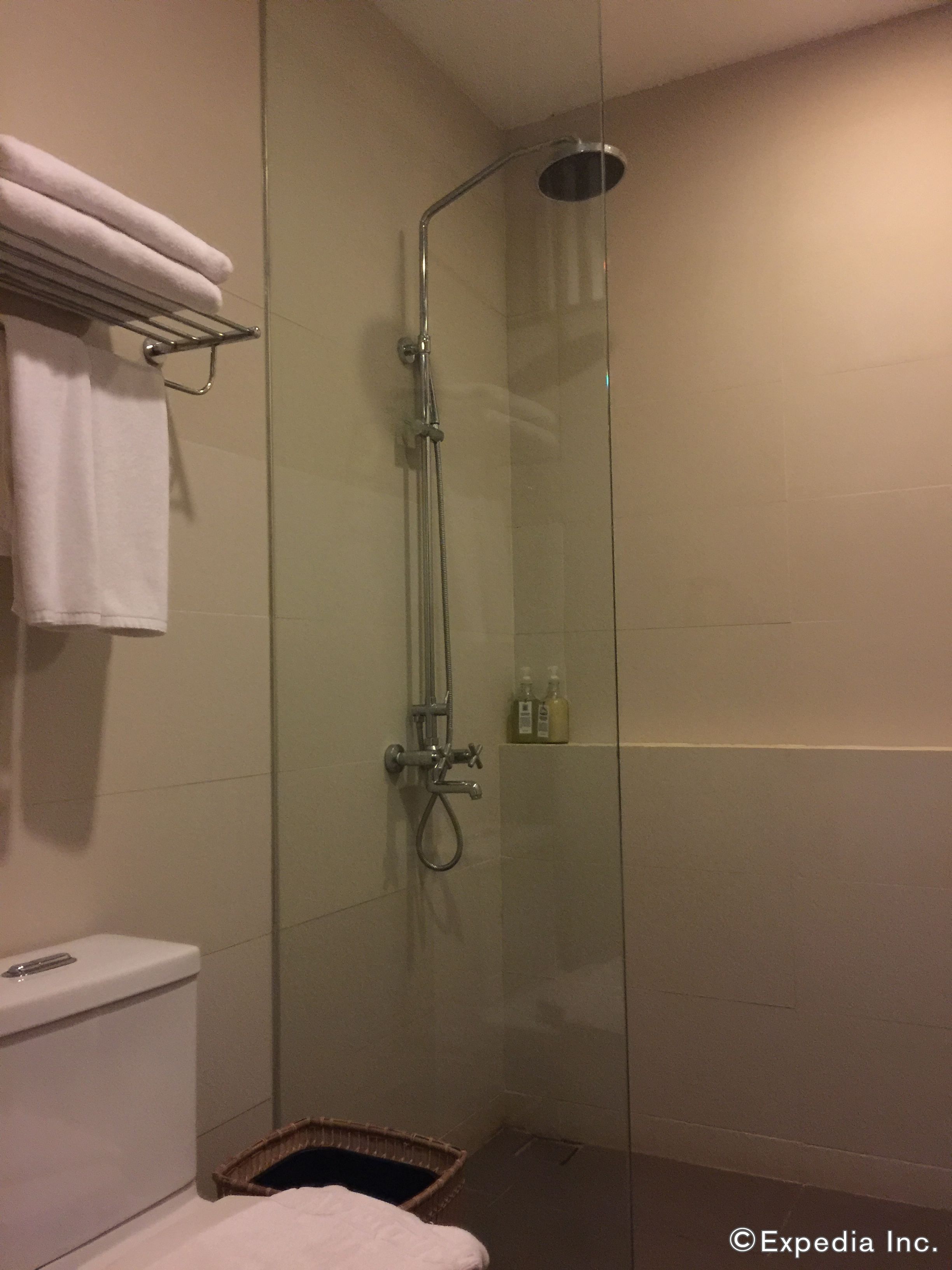 A glass-enclosed shower with a handheld showerhead, a towel rack with folded towels, and a small basket on the floor.