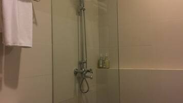 A glass-enclosed shower with a handheld showerhead, a towel rack with folded towels, and a small basket on the floor.