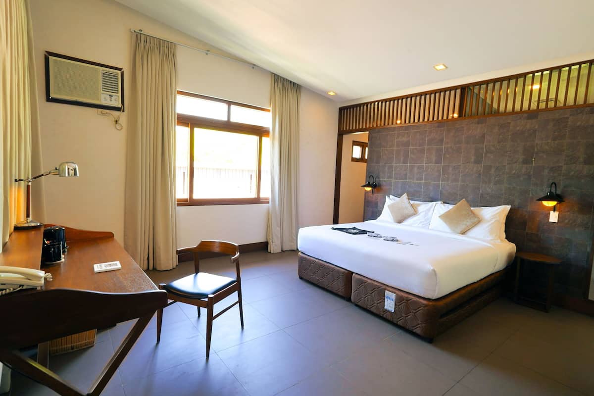 A hotel room with a bed, a desk, a chair, a window, and a wall-mounted air conditioner.