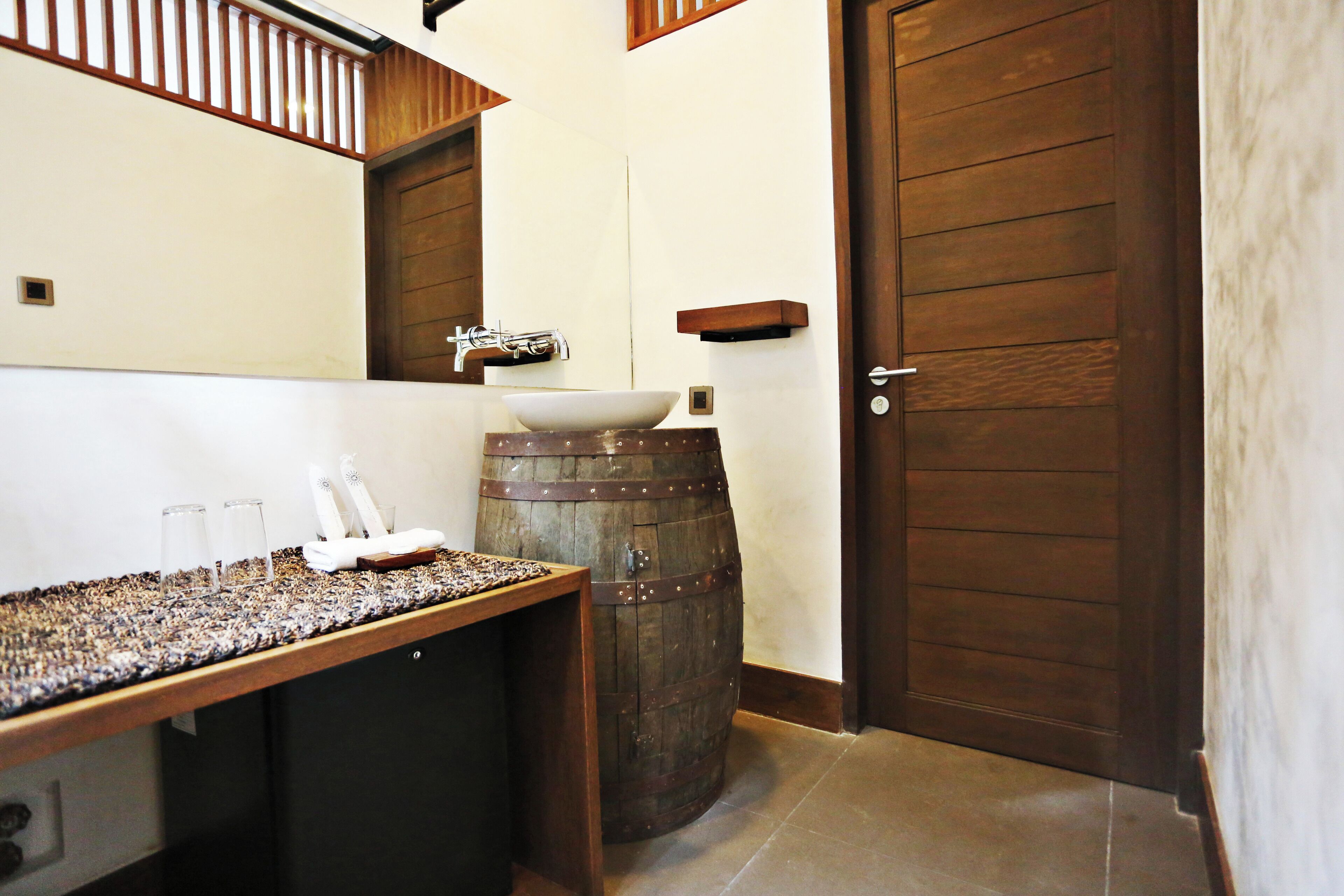 Un baño con un lavamanos de barril de madera, una puerta de madera y una encimera con un vaso.