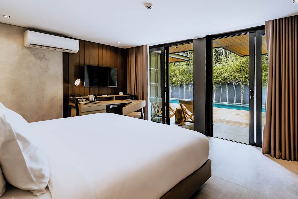 A modern hotel room with a large bed, a desk, a flat-screen TV, and a sliding glass door leading to a pool area.