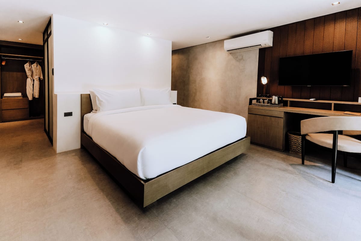 A modern hotel room with a large bed, a desk with a chair, a TV, and a wardrobe.