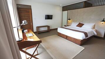 A hotel room with a bed, desk, chair, lamp, TV, and a large mirror.
