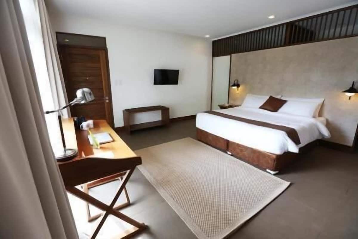 A hotel room with a bed, bedside lamps, a desk with a chair, a TV, and a window with curtains.