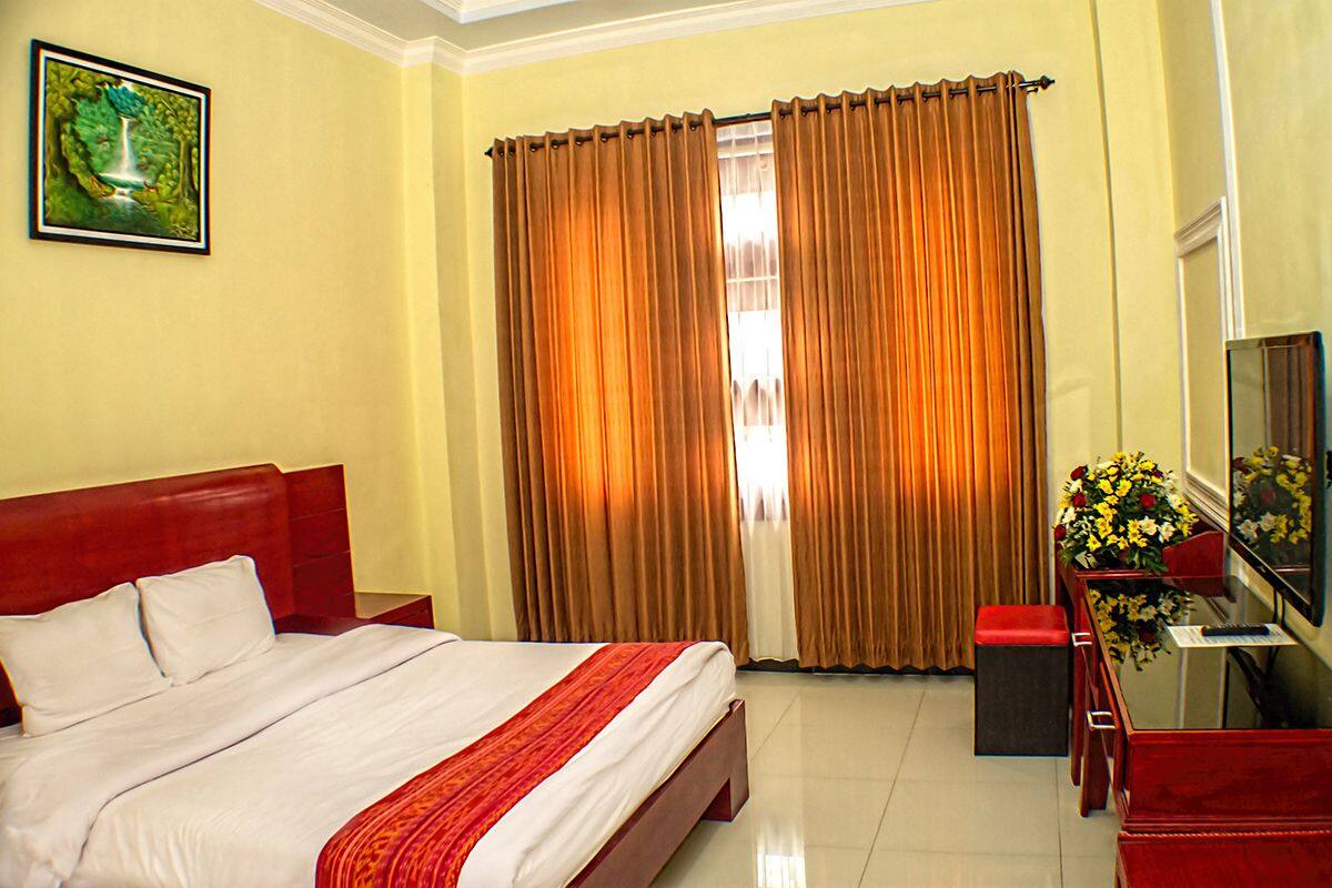 A hotel room with a bed, a desk with a TV, a chair, and a window with curtains.
